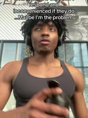 A man with dark skin is centered in a vertical frame. He wears black headphones and a sleeveless black shirt, holding a black water bottle in his right hand. His expression is focused, and he seems to be looking slightly upwards.