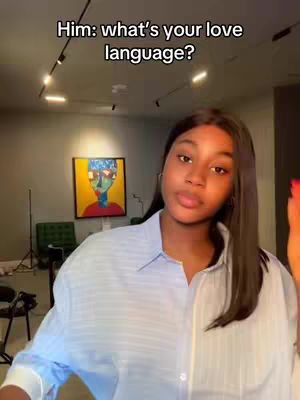 A young woman with long dark hair is centered in the frame, looking towards the camera. She is wearing a light blue collared shirt. The background features a room with neutral-toned walls and artwork. Text overlay indicates a conversation about love languages.