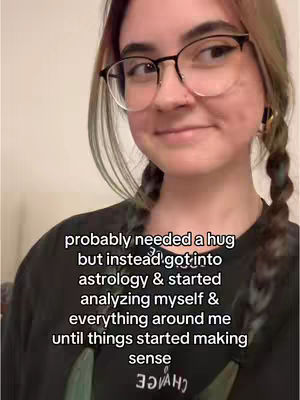 A woman with black-framed glasses and pigtail braids smiles, looking slightly to the side. The text overlayed text reads 'probably needed a hug but instead got into astrology & started analyzing myself & everything around me until things started making sense'.