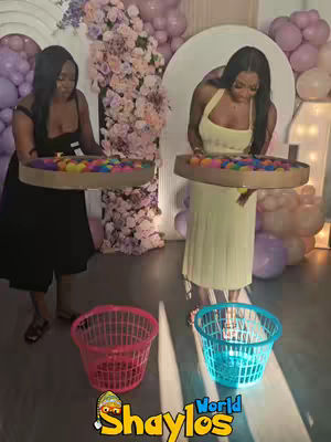Two women are shown in an indoor setting, possibly at a decorative event. Each holds a tray filled with colorful balls, seemingly part of a game. Below each woman, there's a colorful laundry basket. The background includes floral arrangements and balloons.