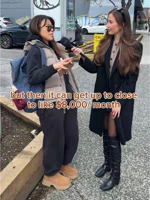 Two women are standing outdoors, one is holding a microphone and interviewing the other. The woman with the microphone is wearing a black coat, black boots, and has sunglasses on her head. The woman being interviewed is wearing a backpack, a vest, and is gesturing with her hands. Text is overlaid on the image.