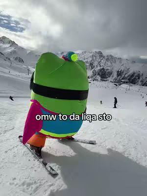 A person in a colorful costume is skiing down a snowy slope with a mountain backdrop and a cloudy sky. Text overlay 'omw to da liqa sto'.