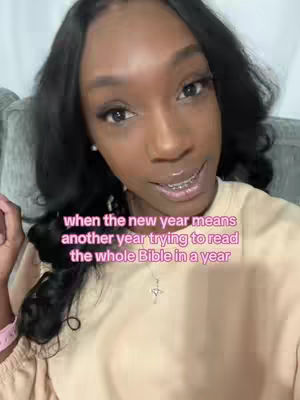 A selfie-style shot featuring a Black woman with long, black hair and delicate jewelry, set against a soft, blurred background. The text overlay states, “when the new year means another year trying to read the whole Bible in a year”. The woman’s expression suggests thoughtfulness.