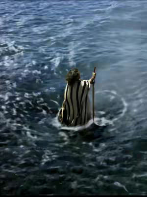 An image captures a figure, seen from the back, standing in water that appears to be the ocean. The person, dressed in a striped garment, holds a staff or pole. The water is a mix of blues and greens, with waves and a sense of depth.