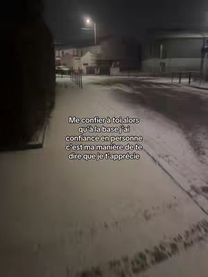 A nighttime street scene covered in snow. The ground and some buildings are visible, with a street lamp illuminating the area. Text is overlaid on the image.