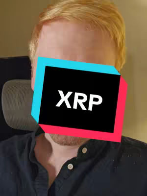 The image is a selfie-style shot focusing on a man's face. A large, rectangular graphic covers the center of the face, featuring the text 'XRP' in white capital letters against a black background. The graphic is outlined with cyan at the bottom and red at the top. The man has fair skin and light-colored hair. He is wearing a black button-down shirt. The background is indistinct with a neutral color.