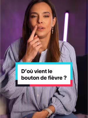 A woman with long brown hair is in a close-up shot, pointing to her nose with her finger. She wears a striped blue and white button-down shirt. A text overlay in a blue box with white text in the bottom center says, "D'où vient le bouton de fièvre ?". In the background, a blurred purple light can be seen.