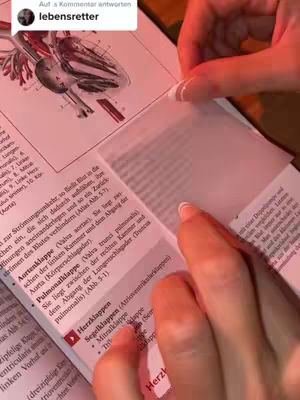A person's hands are holding a transparent sticky note over an open book. The book is open to a page with medical diagrams and German text. The lighting is pink, comment from user lebensretter.