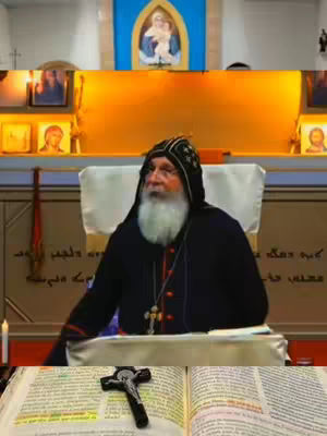 The image features a religious figure in clerical attire seated in front of an altar. The background shows religious iconography, including a depiction of the Virgin Mary and baby Jesus. In the foreground, an open book and a crucifix are visible. The composition is well-lit and focuses on the central figure, suggesting a sermon or religious message.