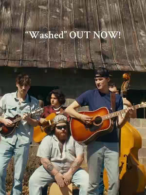 The cover image shows a band of five men outdoors. The band is composed of five men. The background shows a building facade made of wooden boards of different textures. The primary focus is on the band members. The layout is vertically oriented. The lower part of the image portrays the band members. The group is in front of a background in warm muted colors. The colors seem neutral with wooden tones and blues. The lighting is natural looking at the images.