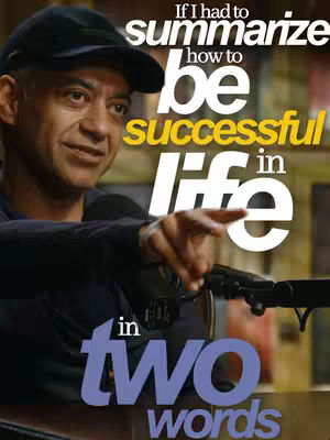 A man in a black cap and dark clothing is the main subject. Text overlays read "If I had to summarize how to be successful in life in two words". The composition is a medium shot with the man slightly off-center, pointing with his right hand. The background is blurred, with warm tones of yellow and brown.
