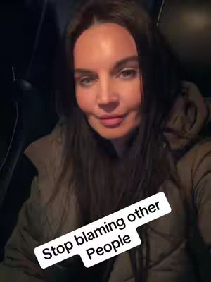 A selfie-style shot featuring a woman inside a car. She's positioned with the camera at eye level, and is looking directly into the camera with a soft smile. The backdrop is a dark interior. The text overlay reads 'Stop blaming other people'.