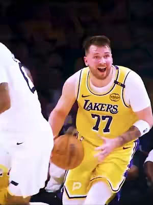 The cover image captures a moment from a basketball game. The central figure, likely Luka Dončić, is shown mid-action with a basketball in his right hand. He's wearing a yellow Los Angeles Lakers jersey with the number 77 prominently displayed. Adjacent to him and slightly out of focus the white shirt and arm of another player.