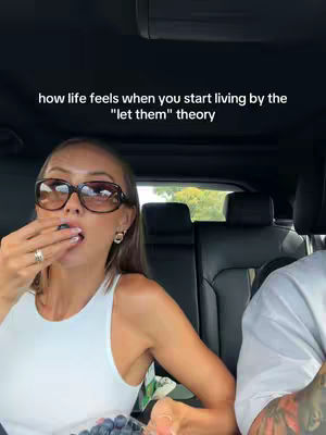 A woman in sunglasses sits in a car, eating a blueberry, with a caption overlaying the top