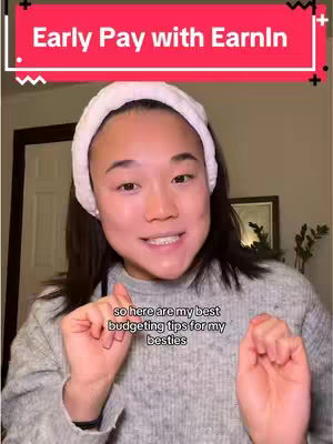 A selfie-style shot featuring a young woman with light skin and dark hair pulled back by a white headband. She's smiling and holding up both hands near her face with her fingers making contact. Text overlay is present at the top of the image and near the bottom. The background appears to be a cozy indoor setting.