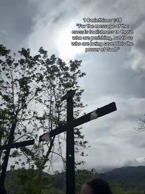 The image shows a landscape with crosses and text overlaid. Several black crosses are in the foreground, with a cloudy sky and trees in the background. Text includes a Bible verse.