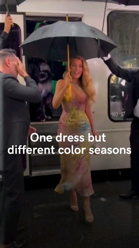 The cover image shows a woman, likely Blake Lively, in a colorful, sparkling gown, walking from a white vehicle with an umbrella overhead. The scene appears to be outdoors, possibly in a city setting, with people in suits around her, with black umbrellas offering protection from the rain.