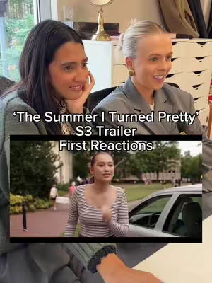 Two women are smiling while watching a video, and a second video is playing with a woman walking out of a building and into the street.