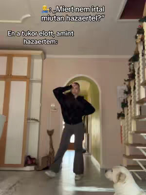 A young woman in a dark jacket and grey pants dances in a well-lit room. The background includes a doorway and stairs. A dog is visible on the floor.