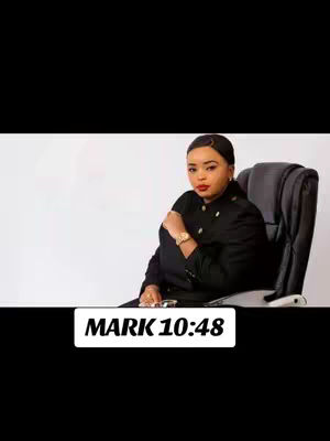 A woman in a black blazer sits in a black office chair against a white background. She has short hair, red lipstick, and is wearing a gold watch. There is text in a white box at the bottom that says 'MARK 10:48.'