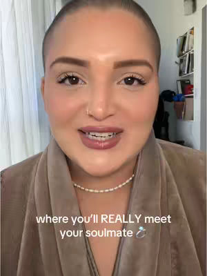 A close-up shot of a woman's face speaking toward the camera. She has short, shaved hair and is wearing a brown wrap. The overlay text says, 'where you'll REALLY meet your soulmate' with a ring emoji.