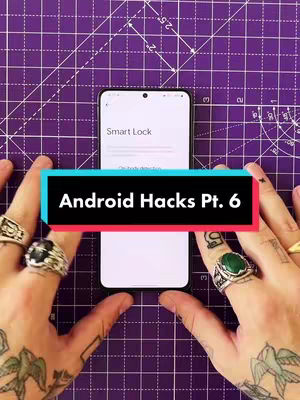 The cover image shows a top-down view of a smartphone held against a purple grid-lined surface.  Hands with multiple rings and tattoos frame the phone from the sides.  A horizontal banner in the foreground displays the text 'Android Hacks Pt. 6'.