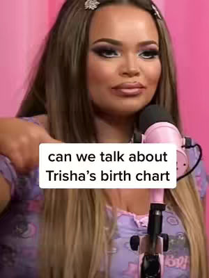 The cover image features a woman with long, light brown hair and full makeup, including prominent eyeshadow. She is holding a pink microphone with her hands and wearing a light purple top possibly adorned with a print that can not be entirely seen in the image. A text overlay in a white box reads, "can we talk about Trisha's birth chart." The background is a solid pink.