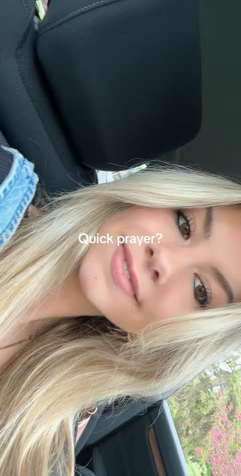 A selfie-style shot featuring a young woman inside a car. She has long blonde hair, fair skin, and is looking at the camera. The text overlayed on the image reads "Quick prayer?". The background shows the interior of the car, including the seat and outside foliage.