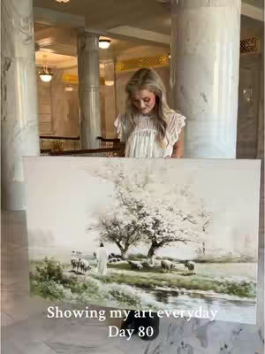 A woman stands in an elegantly designed hall, partially obscuring a large painting depicting a pastoral scene. The artwork presents a tranquil view with figures in white robes, sheep grazing on a green landscape, and two large trees. The setting is bright and airy, with the woman and art piece as the main elements of focus.