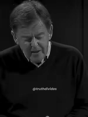 A black and white image featuring a middle-aged man in a dark sweater. The man is seen from the chest up, with his head slightly tilted down and eyes closed. His expression suggests reverence or deep thought. The background is dark and blurred.