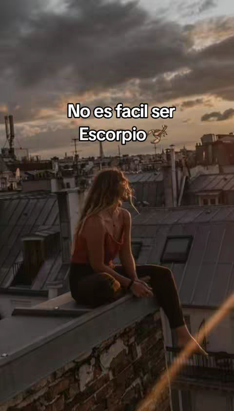 A person is sitting on a rooftop at dusk. The sky has a beautiful array of colors, transitioning from orange to purple, with dark clouds above. The person is seen from behind; the long hair is flowing in the air.  Above the person, the white text "No es facil ser Escorpio" is written in the middle of the frame. A cartoon style scorpion is placed on the right.