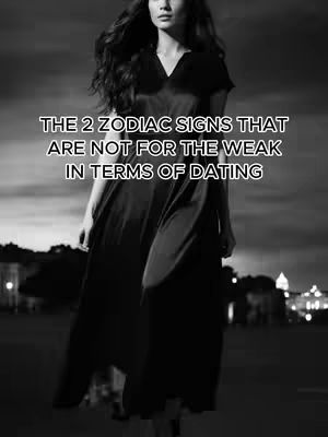 A black and white photo featuring a woman walking towards the perspective of the camera. She is wearing a long, dark dress and the background is slightly out of focus, suggesting an urban setting with lights.