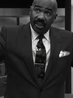 Black and white image featuring a man, Steve Harvey, wearing a dark suit, white shirt, and a patterned black tie. The text "like" is overlaid onto the image.