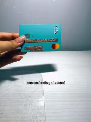 A hand holding a teal credit card with glittered accents and the words, "une carte de paiement" overlaid at the bottom.
