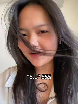 A young woman with long, dark hair partially covering her face, looking slightly to the side with a soft expression. Overlayed text appears near her mouth. The background is a neutral, possibly indoor setting.