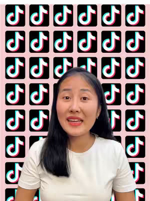 A woman with long dark hair appears in the center of the frame, smiling and speaking. Behind her, a pattern of numerous TikTok logos fills the background, set against a light pink backdrop. She is wearing a white t-shirt.