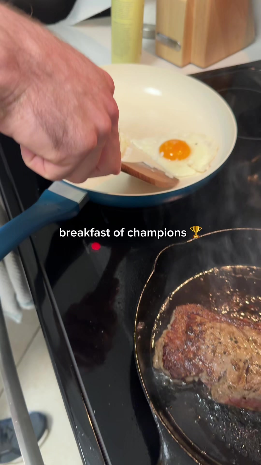 A cooking scene with a close-up view of a person's hand flipping an egg in a white pan, with steak cooking in a separate pan with focus on the food being made. The hook text is added at the bottom.