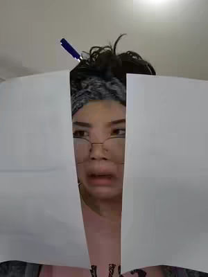 A woman with glasses framed by two white papers, her expression of confusion. A pen partially enters from above. The background shows a plain wall.