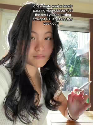 A young woman with long black hair is the focal point. She is seated near a window with natural light, holding an object in her right hand. Text overlays the top, offering motivational advice in a casual, encouraging tone.