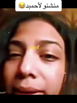 A close-up selfie of a woman with brown hair, looking at the camera with a slight expression. The image is dominated by her face, with the top of her head and a bit of her neck visible. The background is neutral in color, with hints of what appears to be a wall or room. In the top left is a white box with arabic text and a laughing emoji.