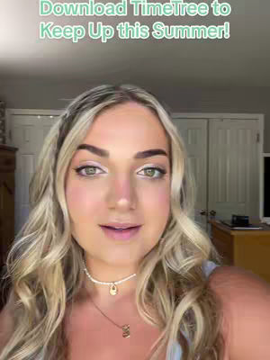 Close-up shot of a woman with blonde wavy hair looking directly at the camera. She is wearing makeup and a necklace. The background shows a glimpse of a room.