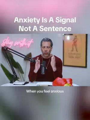 The cover image features a man in a maroon long-sleeved shirt, seated at a desk with a microphone. Above, the text "Anxiety Is A Signal Not A Sentence" is displayed in white. The man has his hands up as if he is making a point, with the phrase "When you feel anxious" at the bottom.