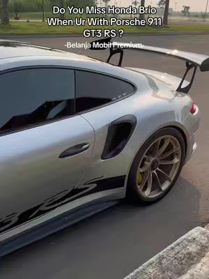 The cover image shows a silver Porsche 911 GT3 RS parked on a paved area. The car is angled, emphasizing its rear with the large spoiler. Text overlays the image with a question about missing a Honda Brio, suggesting a comparison. The overall composition draws attention to the luxury sports car, highlighted by the sleek design and the setting.