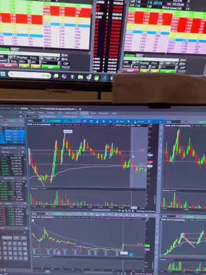 The image focuses on multiple computer screens displaying stock market data and trading interfaces. The layout presents a variety of charts and financial information, showing green and red lines, indicative of stock movements, with numerical data that likely represents prices, volumes and market activity. The screens suggest a day trading environment with dynamic financial market analysis.