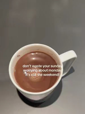 A white mug filled with a brownish liquid, presumably a warm beverage, sits on a plain gray surface. Text in white is overlaid on the image, encouraging the viewer to not worry about Monday.