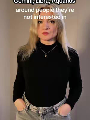 A young woman with blonde hair stands in front of a neutral background. She wears a black long-sleeved shirt and blue jeans, with her hands in her pockets. Text overlays at the top of the image.