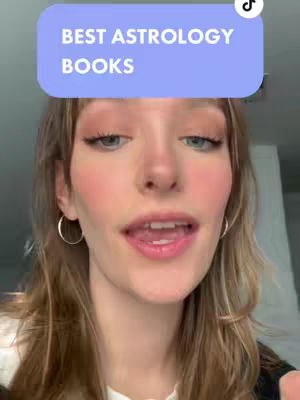 A close-up shot of a young woman with fair skin and long, light brown hair is shown. She is wearing a white shirt and gold hoop earrings. Her facial features, including blue eyes, are in focus, and she is speaking with a slightly open mouth. A light blue rectangle with the text 'BEST ASTROLOGY BOOKS' is positioned above her head. The background is blurred, with glimpses of a white wall.