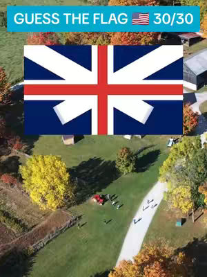 An aerial view shows a green field surrounded by trees with colorful foliage. A flag resembling the British Union Jack is prominently displayed in the center of the image, with text overlays at the top indicating a quiz about flags. Below the flag, a pathway weaves through the field, with a few people scattered around.