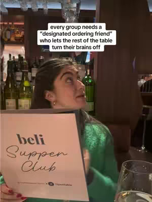 A woman in a green top is holding a menu with the words 'beli Supper Club' while looking up and to the right. Above her head is a text overlay.
