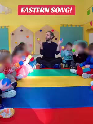 The cover image shows a man sitting cross-legged on a colorful floor in what appears to be a classroom. He's surrounded by children. The man is holding up two small balls, with text overlayed at the top that reads "EASTERN SONG!"